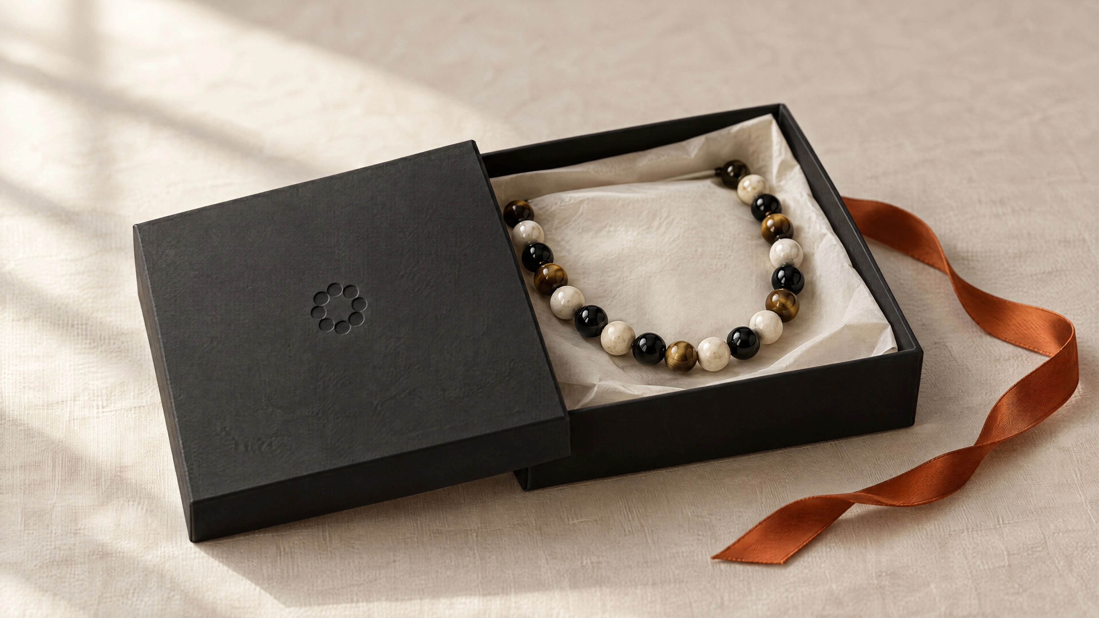 Black GRAIN box with the debossed bead symbol, a stone necklace on tissue and an orange ribbon